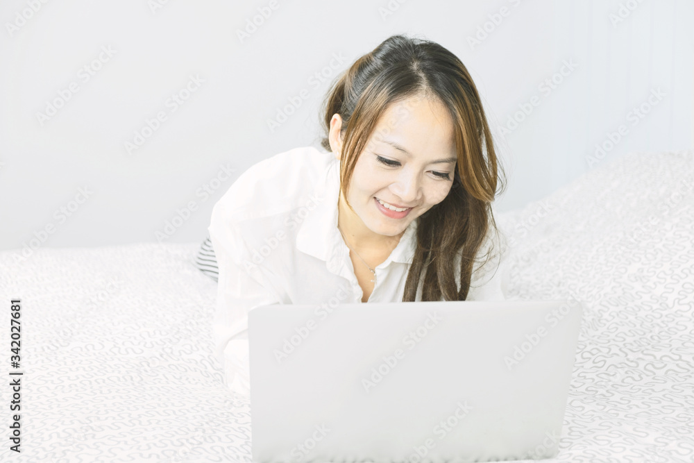 Asian woman using laptop in emotional smile happily while laying on the bed. Lifestyle, Relaxing, Leisure, Technology communication concept. Asian woman using laptop in emotional smile happily while laying on the bed. Lifestyle, Relaxing, Leisure, Technology communication concept.