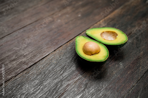 A side view of a ripe avocado halves lying on a wooden brown background with copy space. One slice with core. Fresh food for a great healthy diet.
