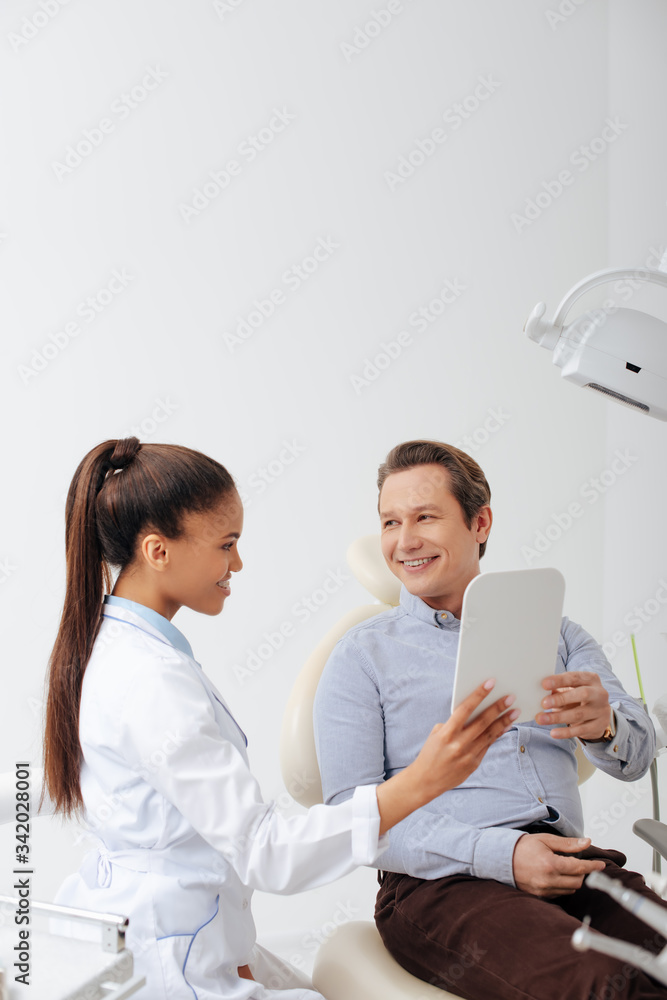 happy patient looking at mirror near smiling african american dentist in braces happy patient looking at mirror near smiling african american dentist in braces
