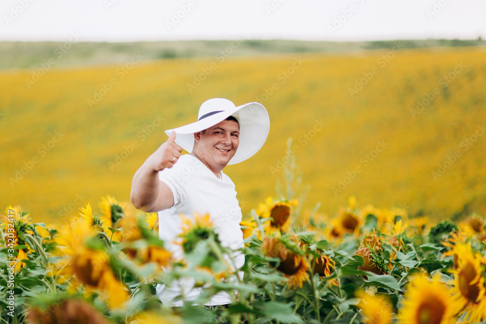 Portrait of a handsome young man in a white woman's hat in a field with sunflowers. Man is having fun outdoors. copy space. selective focus