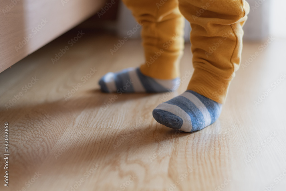 Baby feet with striped socks, standing and trying his first steps, selective focus
