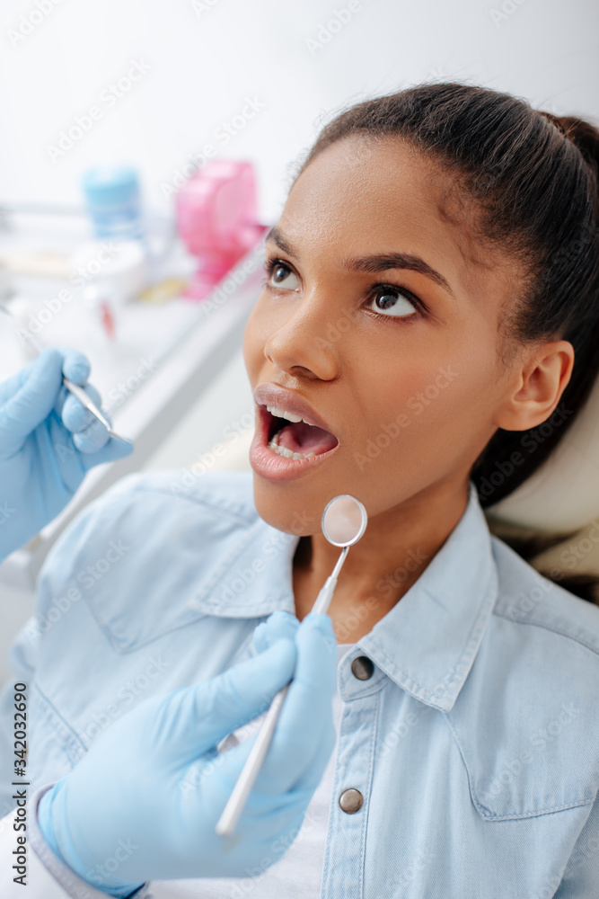 dentist in latex gloves holding dental equipment near african american patient with opened mouth dentist in latex gloves holding dental equipment near african american patient with opened mouth