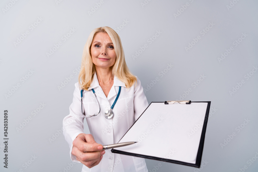 Portrait of experienced retired pensioner woman doc hold clipboard ask patient sign corona virus pneumonia treatment agreement wear white coat isolated over gray color background Portrait of experienced retired pensioner woman doc hold clipboard ask patient sign corona virus pneumonia treatment agreement wear white coat isolated over gray color background