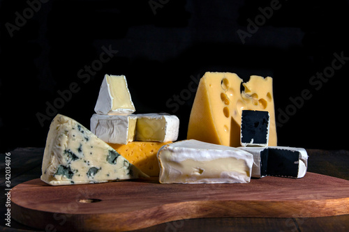 Cheese assortment: blue cheese, hard cheese, soft cheese on a cutting board. Slate black background. Copy space