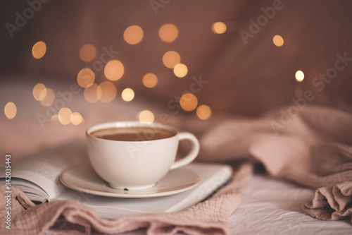 Cup of tasty coffee on paper book over glowing lights closeup. Good morning. Breakfast.