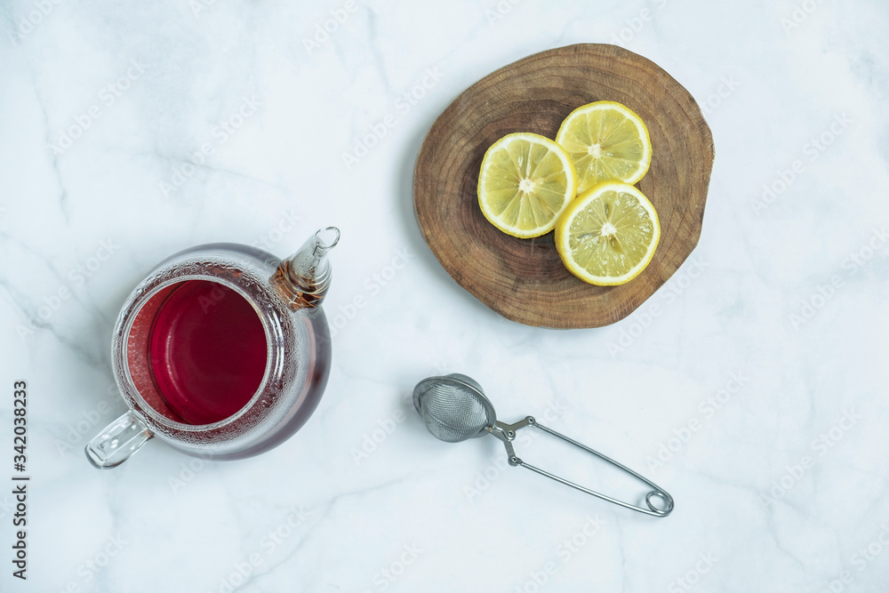 Brewed fresh tea, strainer with a sliced lemon in wooden platter on marble background. Traditional, healthy and organic beverage. Top view, flat lay. Brewed fresh tea, strainer with a sliced lemon in wooden platter on marble background. Traditional, healthy and organic beverage. Top view, flat lay.