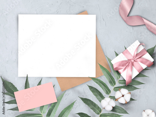 Mock up wedding concept with envelope, gift, ribbon, cotton flowers and leaves on grey background. Elegant still life flatlay for Mothers day, Womans day or wedding invitation.