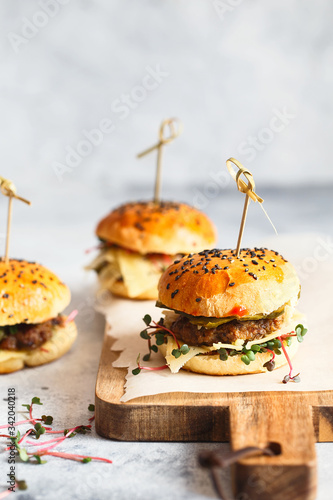 Homemade mini burgers with bamboo brochettes. Sandwiches with meat patties, cheese, pickles and radish microgreens served with fingerfood sticks. Cooking home