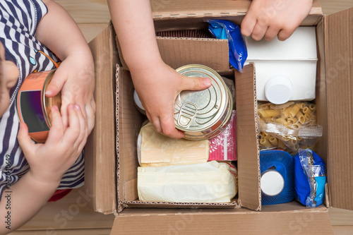 Children opening a food delivery box at home, online ordering. Grocery store delivery. Box full of food in concept donation boxparcel. Delivery during quarantine due to coronavirus COVID-19 disease