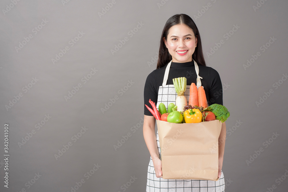 Portrait of beautiful young woman with vegetables in grocery bag in studio grey background Portrait of beautiful young woman with vegetables in grocery bag in studio grey background