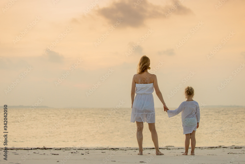 Back view of young mother and her adorable cute little girl holding hands and looking at beautiful ocean sunset. Happy family concept. Back view of young mother and her adorable cute little girl holding hands and looking at beautiful ocean sunset. Happy family concept.