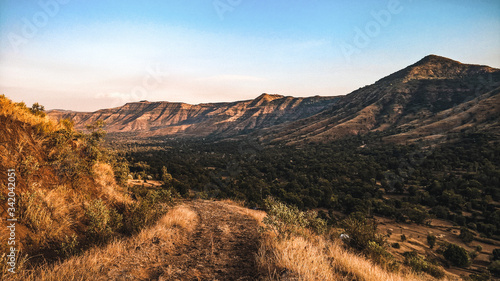 The mighty Sahyadri montains  kissed by the golden rays of the setting sun overlooking a windy trail disappearing into the woods