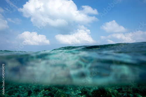 Underwater tropical coral reef splitted by cloudy sky waterline. Beautiful turquoise deep ocean view over and under water surface, Indian ocean, Maldives.