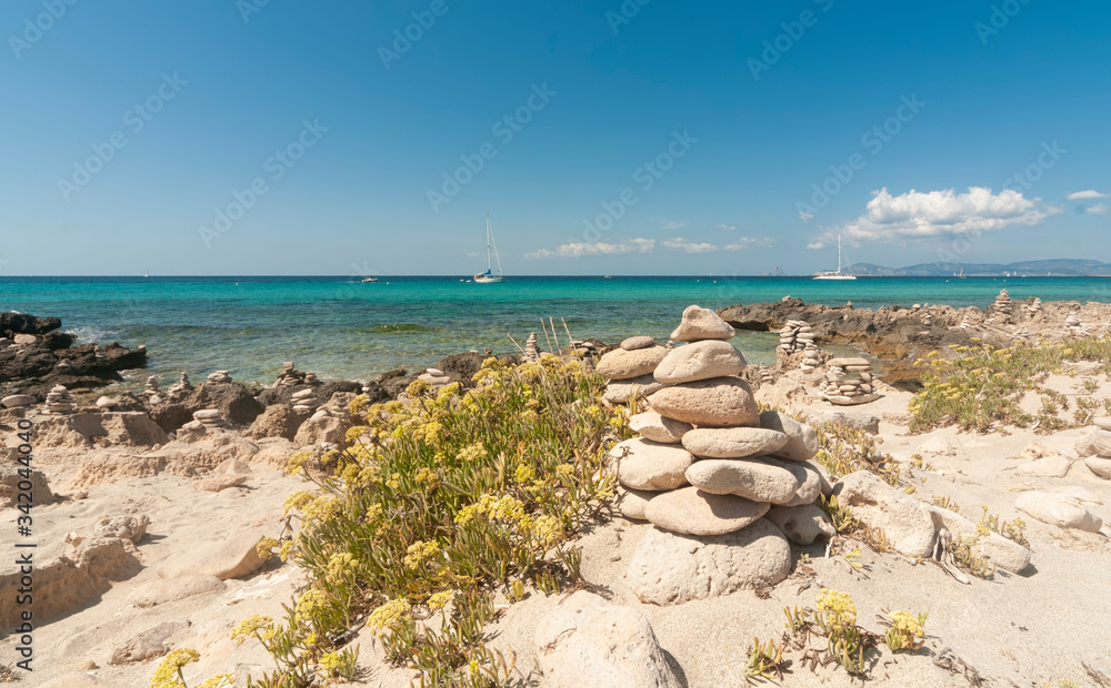 Panoramic view of a sandy and rocky beach. In the background the Mediterranean sea with sailing boats moored on the quiet bay of Formentera, Balearic Islands of Spain, Europe.