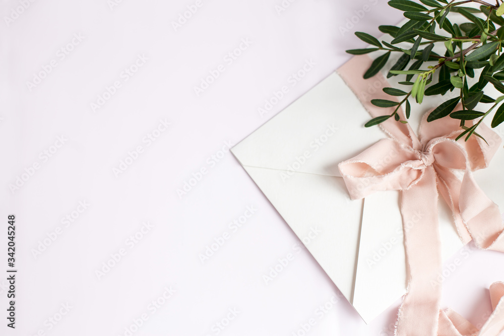 Envelope on a white-pink background with peach silk ribbon and pink flowers. Wedding invitation. Mother's day card. Place for text. Copy space Envelope on a white-pink background with peach silk ribbon and pink flowers. Wedding invitation. Mother's day card. Place for text. Copy space