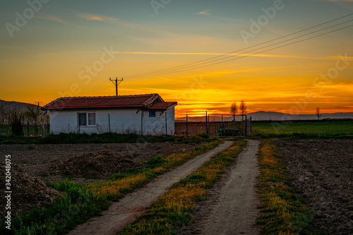 A white country house in the sunset and a dirt road leading to this house