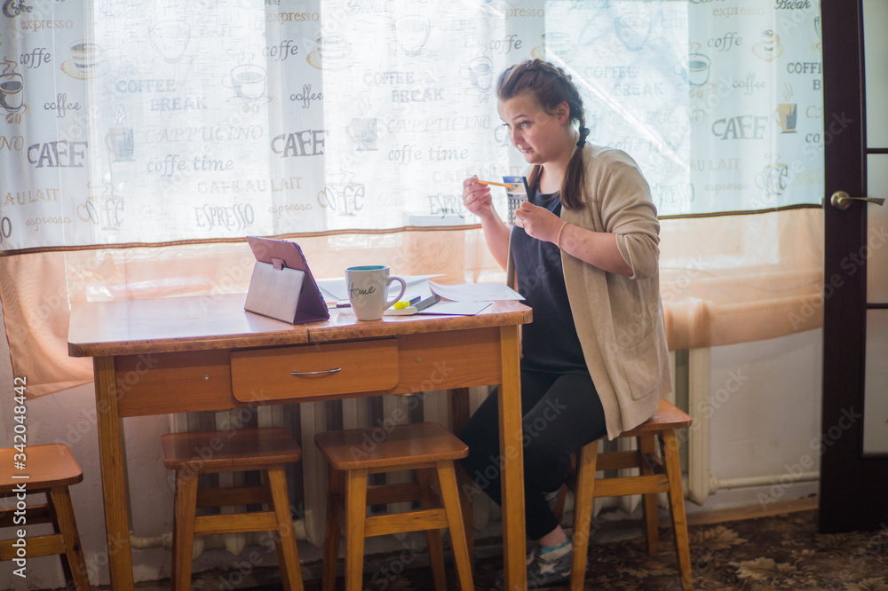 A young girl sits at home in self-isolation and works remotely at home, with finance charts. Communicates via video connection. A young girl sits at home in self-isolation and works remotely at home, with finance charts. Communicates via video connection.