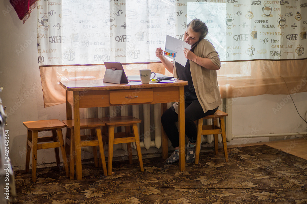 A young girl sits at home in self-isolation and works remotely at home, with finance charts. Communicates via video connection. A young girl sits at home in self-isolation and works remotely at home, with finance charts. Communicates via video connection.