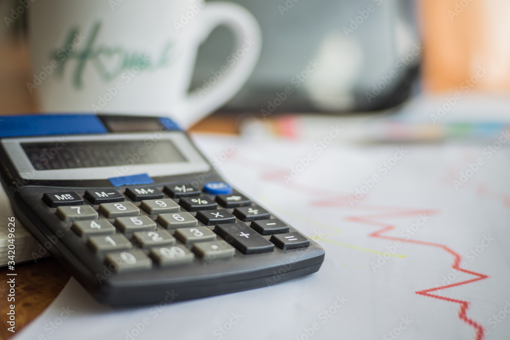 On the home table are stock and finance charts with a calculator, a coffee mug, a pencil, a marker pen, two notebooks, a smartphone and a tablet for remote work. Work at home.