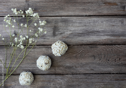 Homemade raw chocolate truffles with nuts and chia seeds in coconut flakes on a wooden background, branch of white wildflowers, horizontal orientation