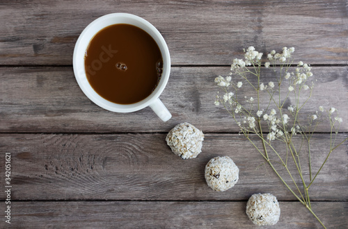 Energy balls on a dark wooden background with a branch of white flowers and a cup of coffee, flat lay, copy space, concept of a healthy quarantine snack