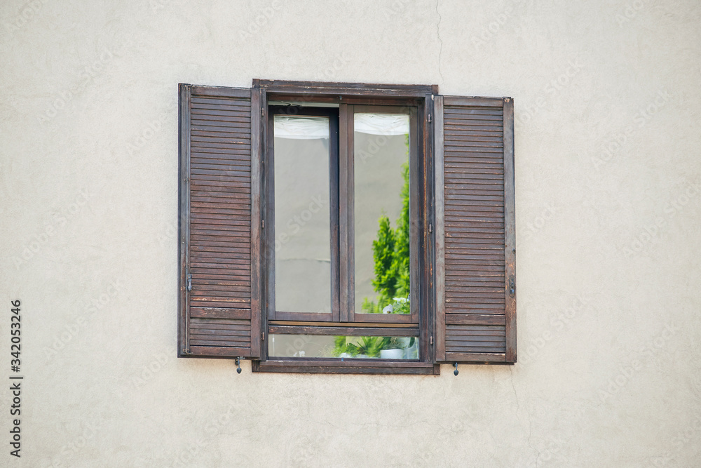 Fototapeta premium Italian window on the sandy yellow wall facade with open brown color wooden classic shutters