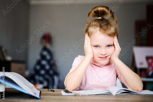 The girl doing homework sitting at home at the table, books and notebooks, on the table is a globe, the concept of distance learning