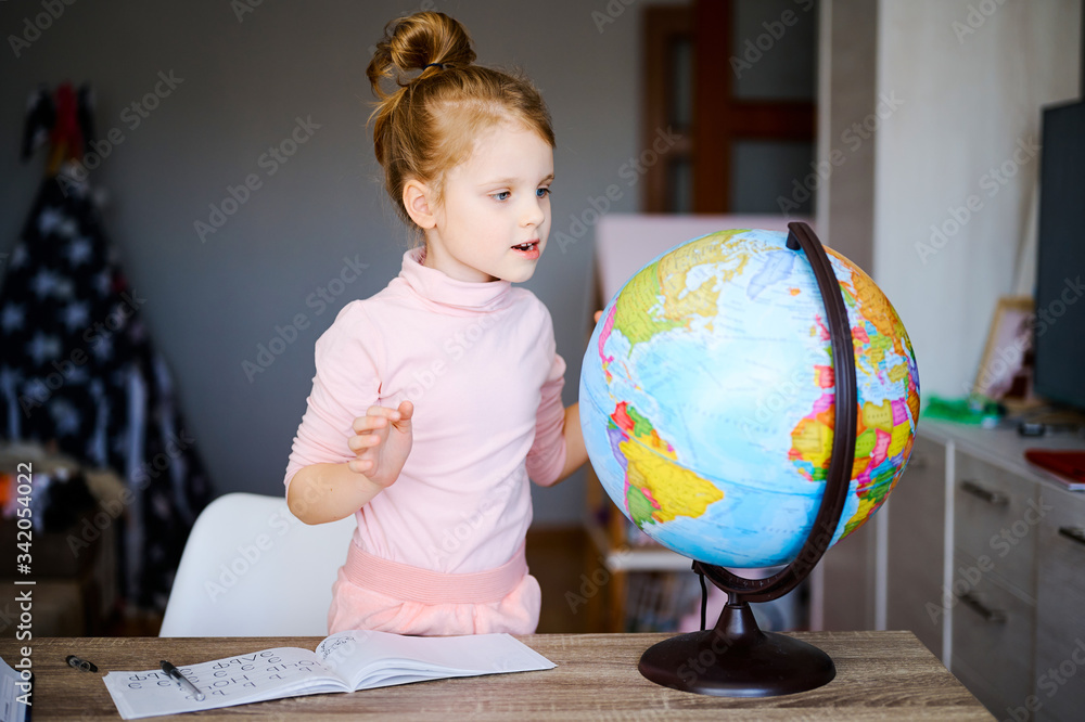 Young caucasian girl looking at earth globe at home. Schoolgirl doing homework and showing something at the globe Young caucasian girl looking at earth globe at home. Schoolgirl doing homework and showing something at the globe