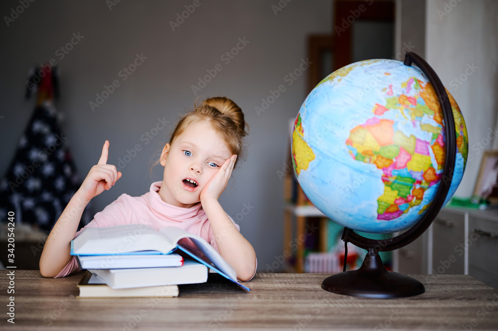 Caucasian schoolgirl shows finger, reading books, doing homework. Training books, notebooks and globe at the table. Distance learning concept, online education Caucasian schoolgirl shows finger, reading books, doing homework. Training books, notebooks and globe at the table. Distance learning concept, online education
