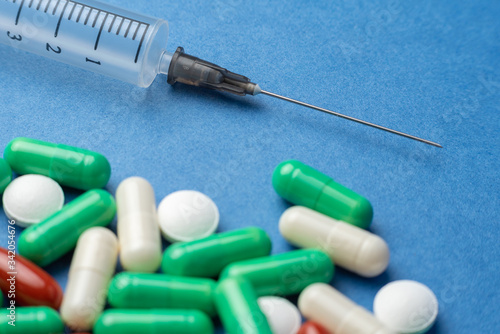 many multi-colored medical antiviral pills with syringe on blue background close-up