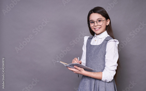 Portrait of a cute Caucasian lady with long dark hair in glasses with a pen and notebook, on a gray background.