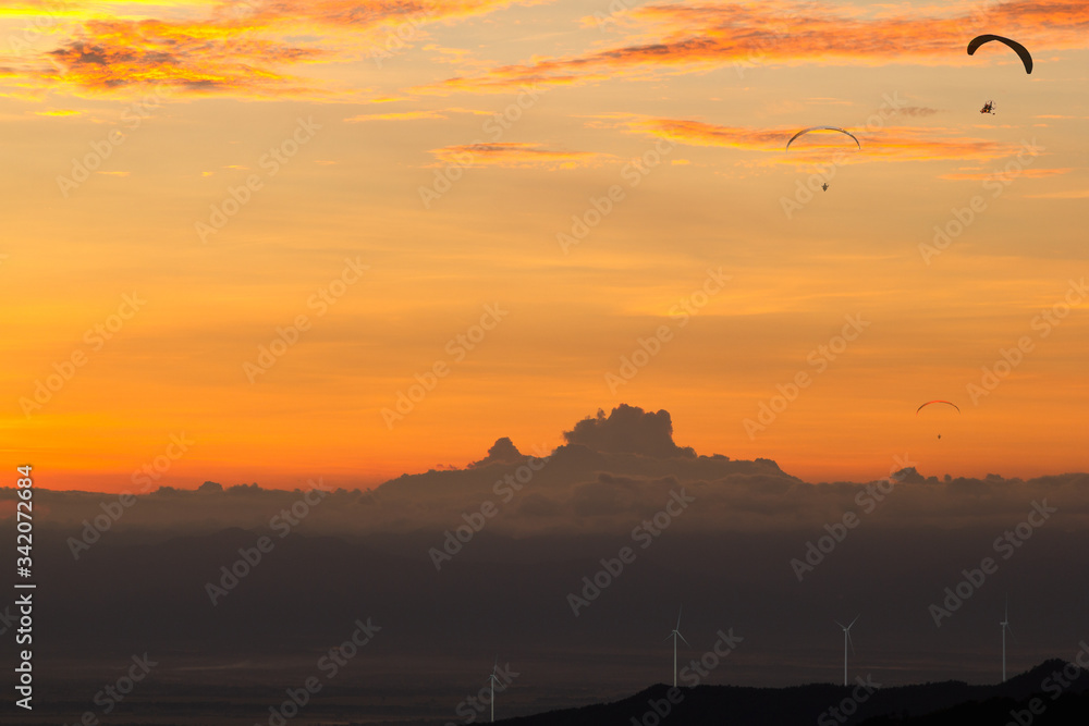 Landscape of Electric wind turbine generator at sunset on hill with dark clound and Powered Parachute Flying background