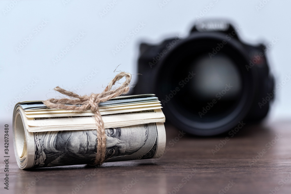 Money (US dollars) in a roll tied with a rope near the camera. Salary for the work of a photographer