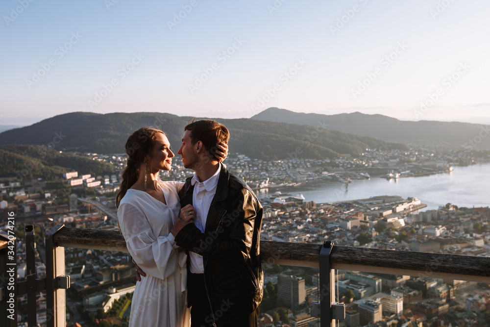 Two lovers standing on the observation deck of Bergen, Norway, against the background of the sunset