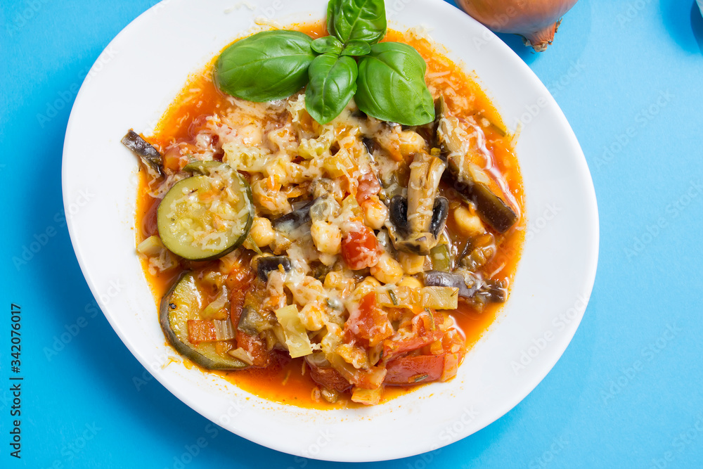 Vegetable stew with eggplant, zucchini, tomatoes and mushrooms. White plate and blue background Vegetable stew with eggplant, zucchini, tomatoes and mushrooms. White plate and blue background
