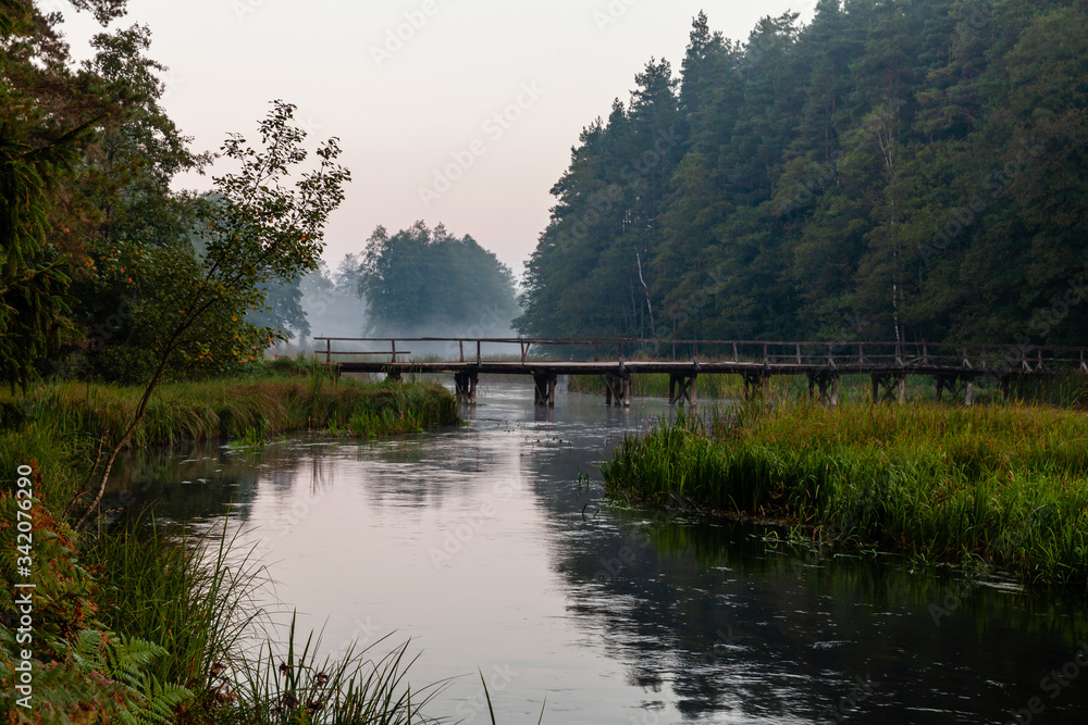 Old wooden bridge over Czarna Hancza river near Sarnetki village. Calm, peaceful morning landscape view. Poland, Europe.