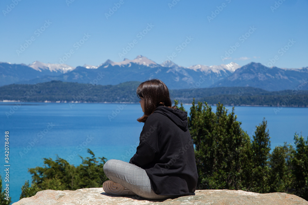 Young girl sitting on a rock look at the lake and mountains. Bariloche, Argentina