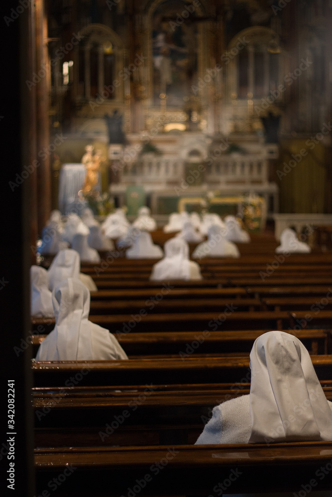 Nuns in white dress praying in Cottolengo's church with sunlight through the windows.
