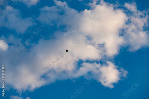 A kite flying high in the sky against beautiful white clouds and blue summer skies.