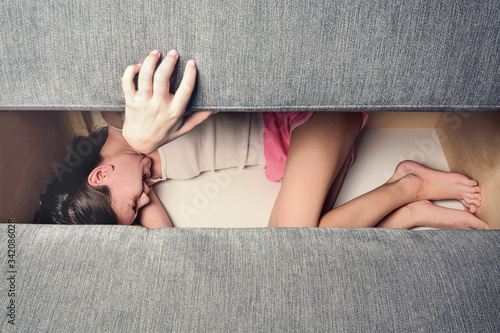 Girl screaming with open mouth hiding in sofa closes it. The concept of child abuse.