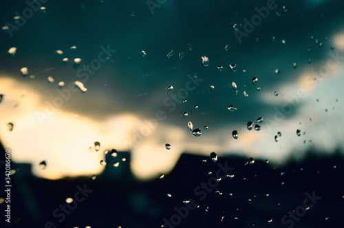 Raindrops on a window in the evening against the background of a blurred city and clouds