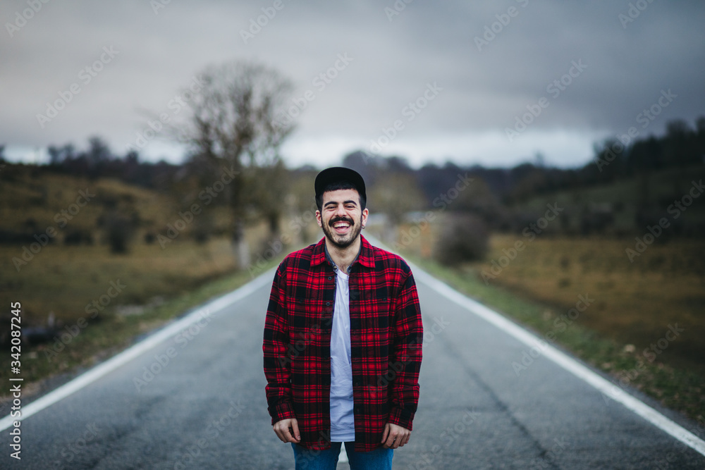 Cheerful man with closed eyes in casual wear standing on empty asphalt road among green fields with cloudy sky on background Cheerful man with closed eyes in casual wear standing on empty asphalt road among green fields with cloudy sky on background