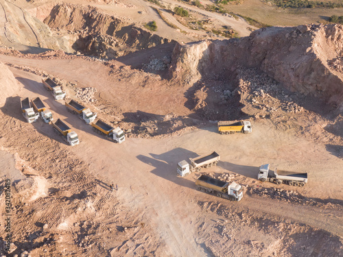 Aerial, flying above stone quarry with working many heavy trucks and machines. Top view, Flight above digging excavators