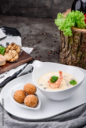 Cream soup with shrimps in white plate and plate with cheese balls on dark concrete background