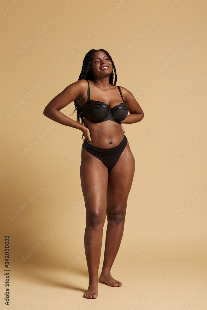 Fotografia do Stock: Curvy beautiful African American woman with braids in  lingerie keeping hands on waist and looking at camera against yellow  background