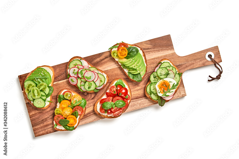 Open sandwiches with avocado, cherry tomato, cucumber, radish. Italian vegan bruschetta on wooden board. Various sandwich with spinach isolated on white, top view. Flat lay