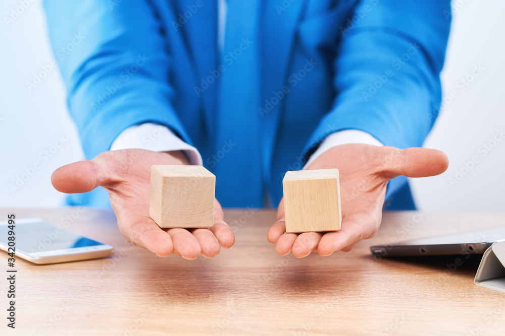 The businessman holds wooden cubes on open palms above the table. There is free space on the blocks for letters, numbers, symbols, or inscriptions. Layout for infographics. The businessman holds wooden cubes on open palms above the table. There is free space on the blocks for letters, numbers, symbols, or inscriptions. Layout for infographics.