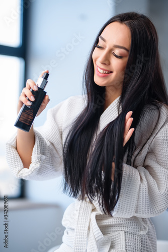 A beautiful brunette girl smiles and sprays herself on her hair in the bathroom. means of hygiene. cosmetics. Body and hair care