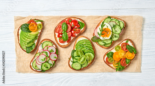 Italian vegan bruschetta on wooden background. Open sandwiches with avocado, cherry tomato, cucumber, radish. Various bruschetta with spinach isolated on white, top view. Flat lay