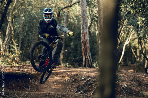Unrecognizable man in helmet, gloves and protection glasses jumping doing whip trick downhill during mountain biking practice in wood forest photo